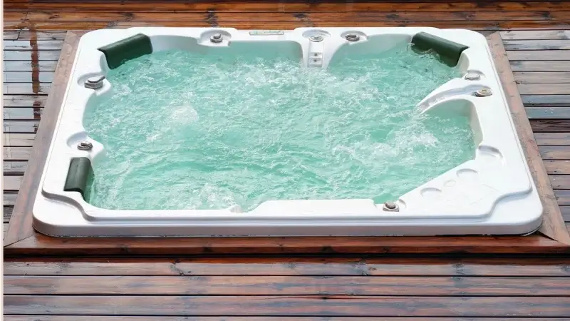 Jacuzzi ogrodowe w drewnianej zabudowie, wypełnione wodą z intensywnie pracującymi dyszami hydromasażu, otoczone tarasem z naturalnych desek.