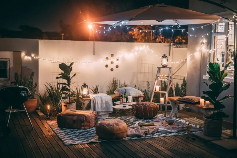 Przytulny taras scandi boho z dekoracyjnym oświetleniem, poduszkami i kocami, przygotowany na wieczorne spotkania.