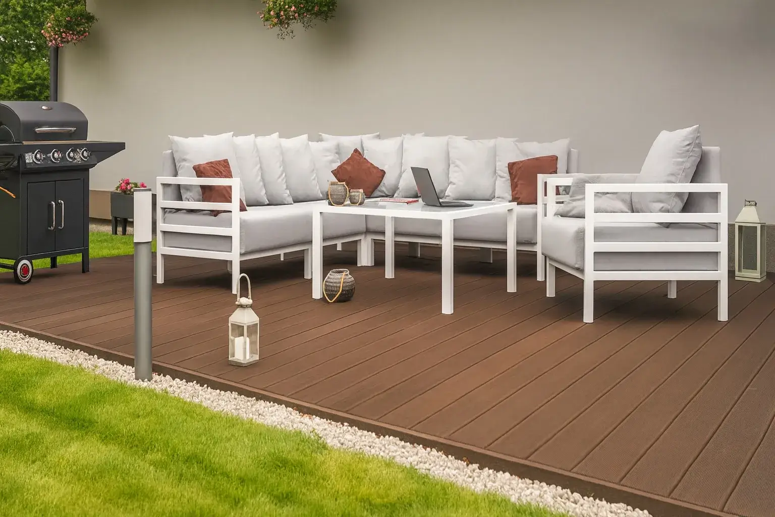 Nowoczesny taras w stylu skandynawskim z białymi meblami ogrodowymi i grillem gazowym, ustawiony na drewnianym podeście, ozdobiony latarniami i poduszkami dekoracyjnymi.