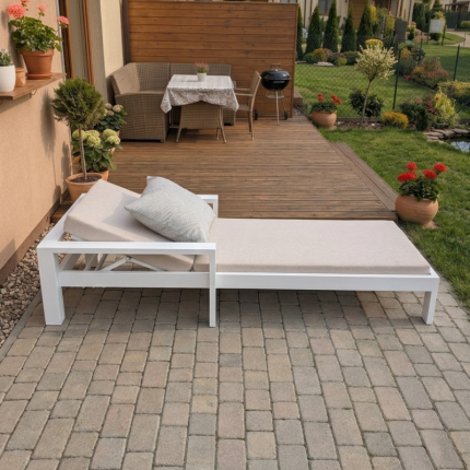 leżak ogrodowy biały z beżowymi poduszkami na tarasie z kostki